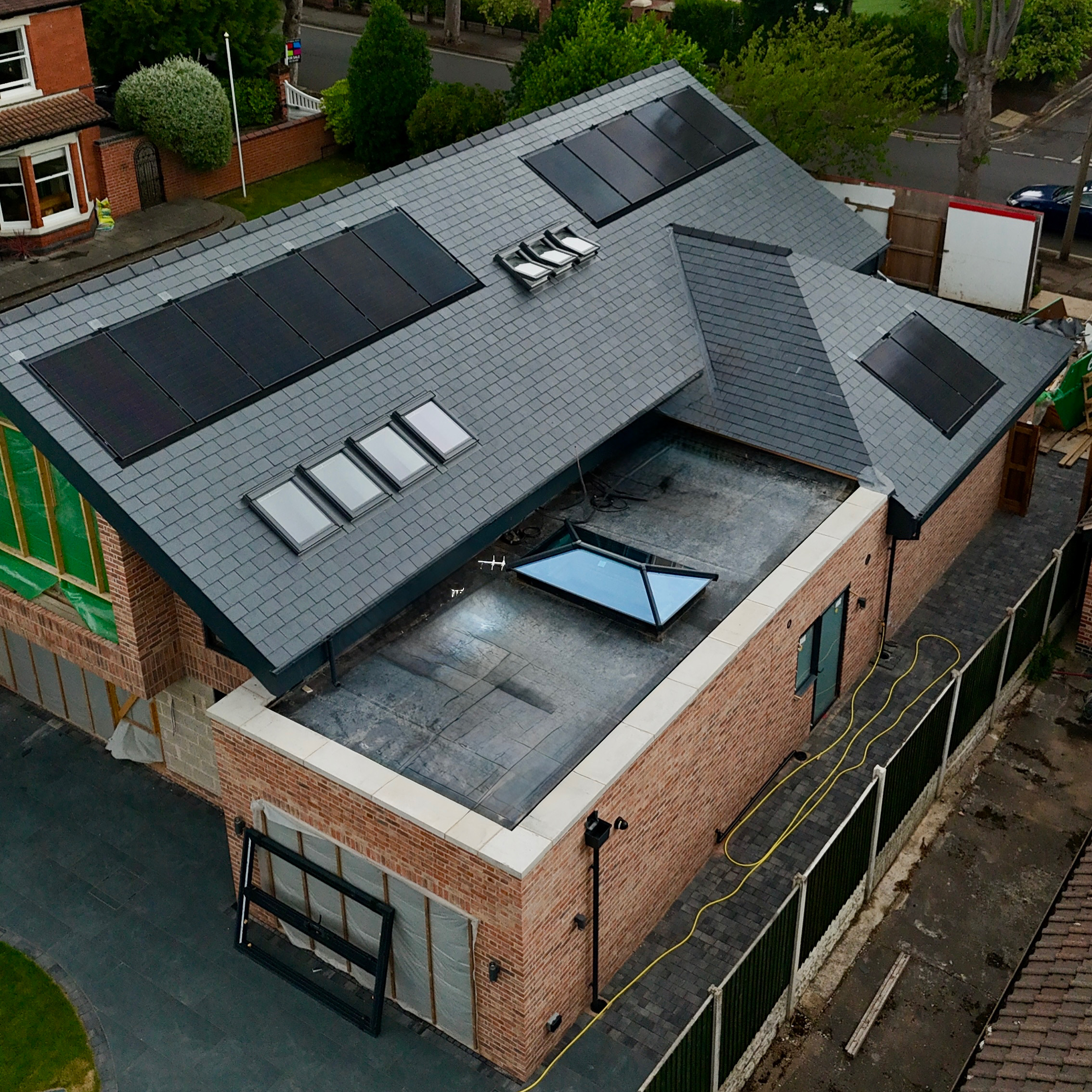 Aerial view of new-build residential property — black solar panels on dark slate roof with flat roof skylight
