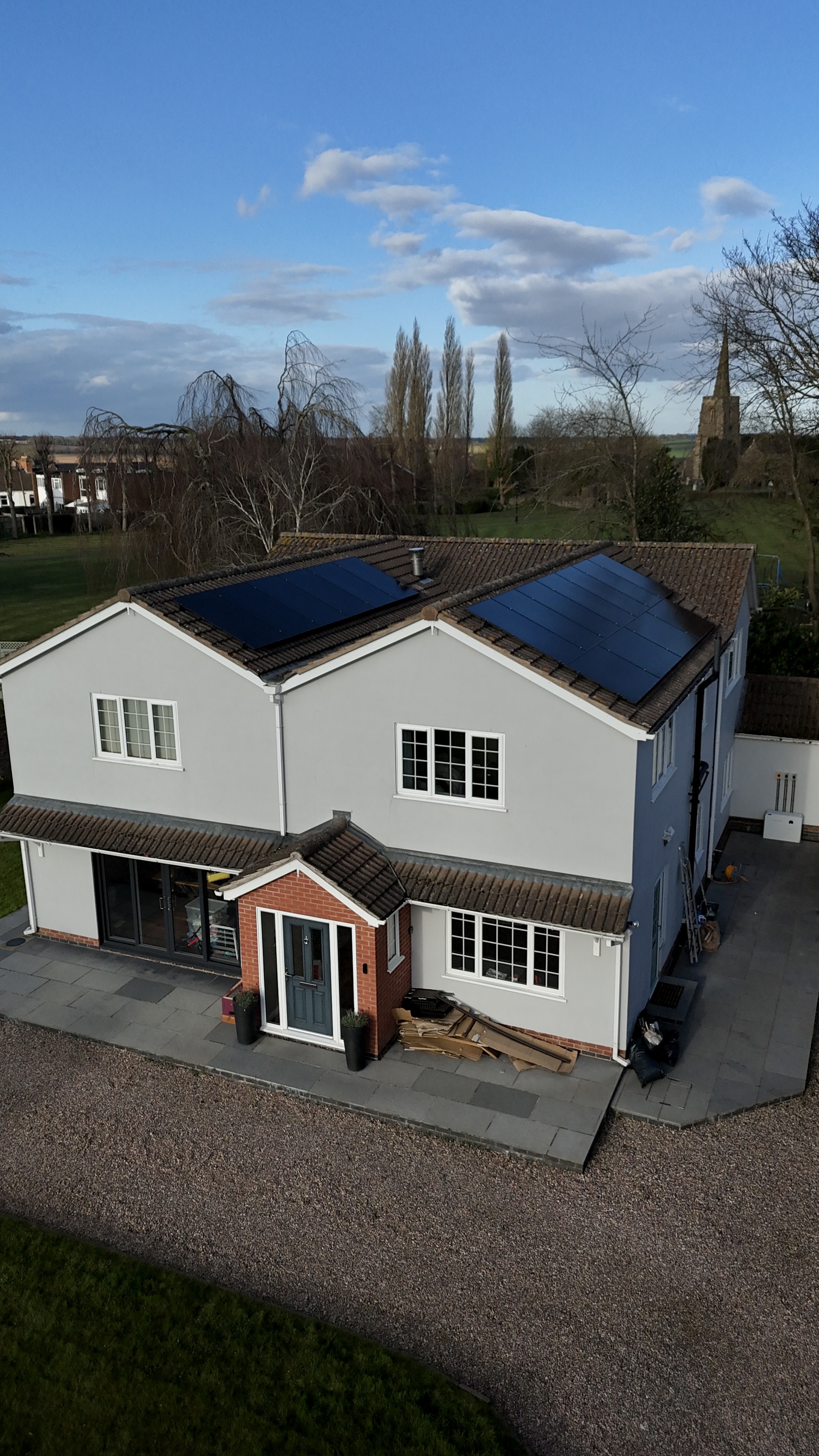 Portrait drone view of large white detached property with completed solar array across both roof pitches